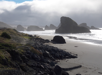 [Sun streaks through dark clouds to light a portion of the ocean, sand, and rock.]